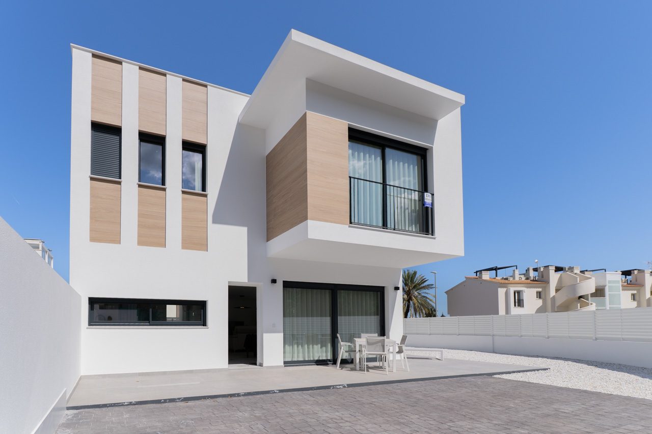 Fachada exterior de diseño contemporáneo con paneles de efecto madera, terraza pavimentada con mobiliario de exterior y amplios ventanales de carpintería negra.