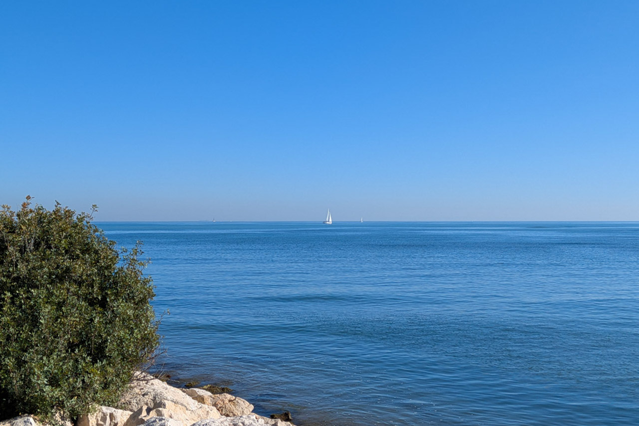 Vista panorámica del mar Mediterráneo desde la costa rocosa de Dénia, con veleros navegando bajo un cielo despejado cerca de la zona de Las Rotas.