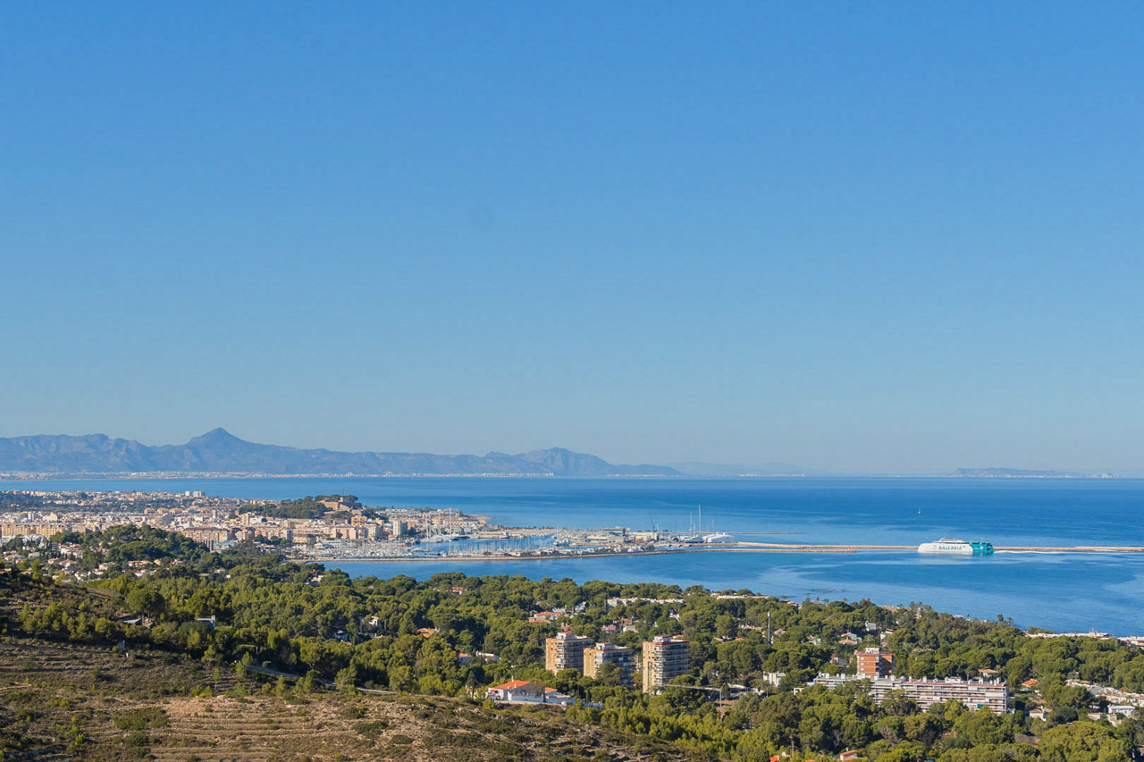 Vista panorámica desde la propiedad hacia el puerto de Dénia y el mar Mediterráneo, con el castillo y la costa de Las Marinas en el horizonte bajo un cielo despejado.