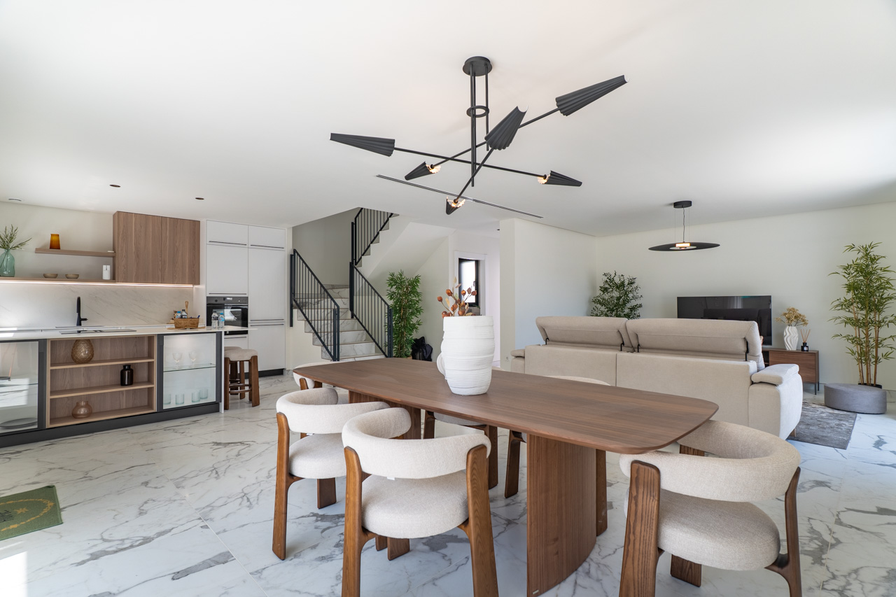 Zona de día diáfana con comedor de diseño, cocina integrada con acabados en madera y mármol, y suelos de gres porcelánico efecto mármol blanco.