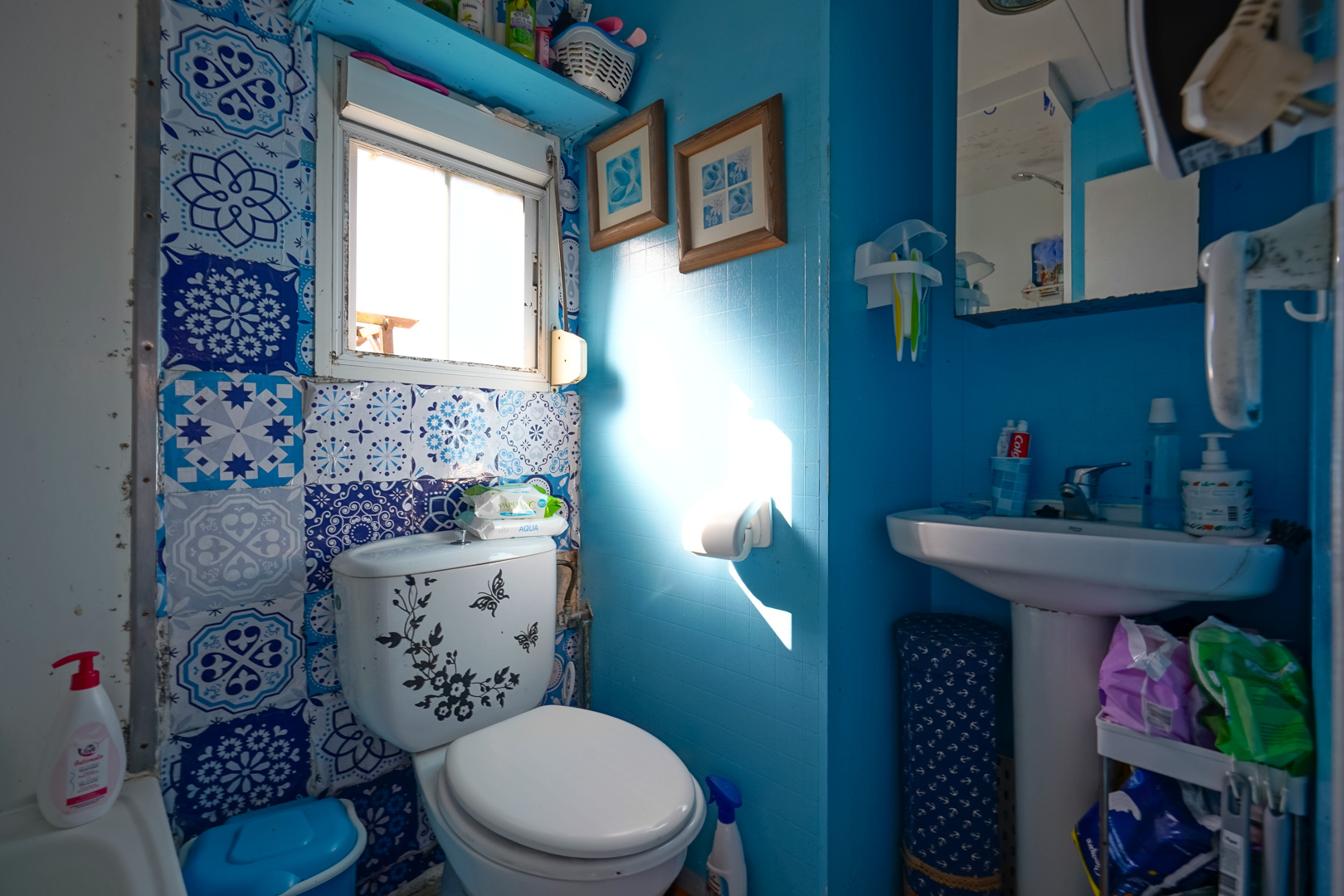 Cuarto de baño compacto con paredes en tonos azules, azulejos decorativos de estilo hidráulico y un lavabo de pedestal bajo luz natural.