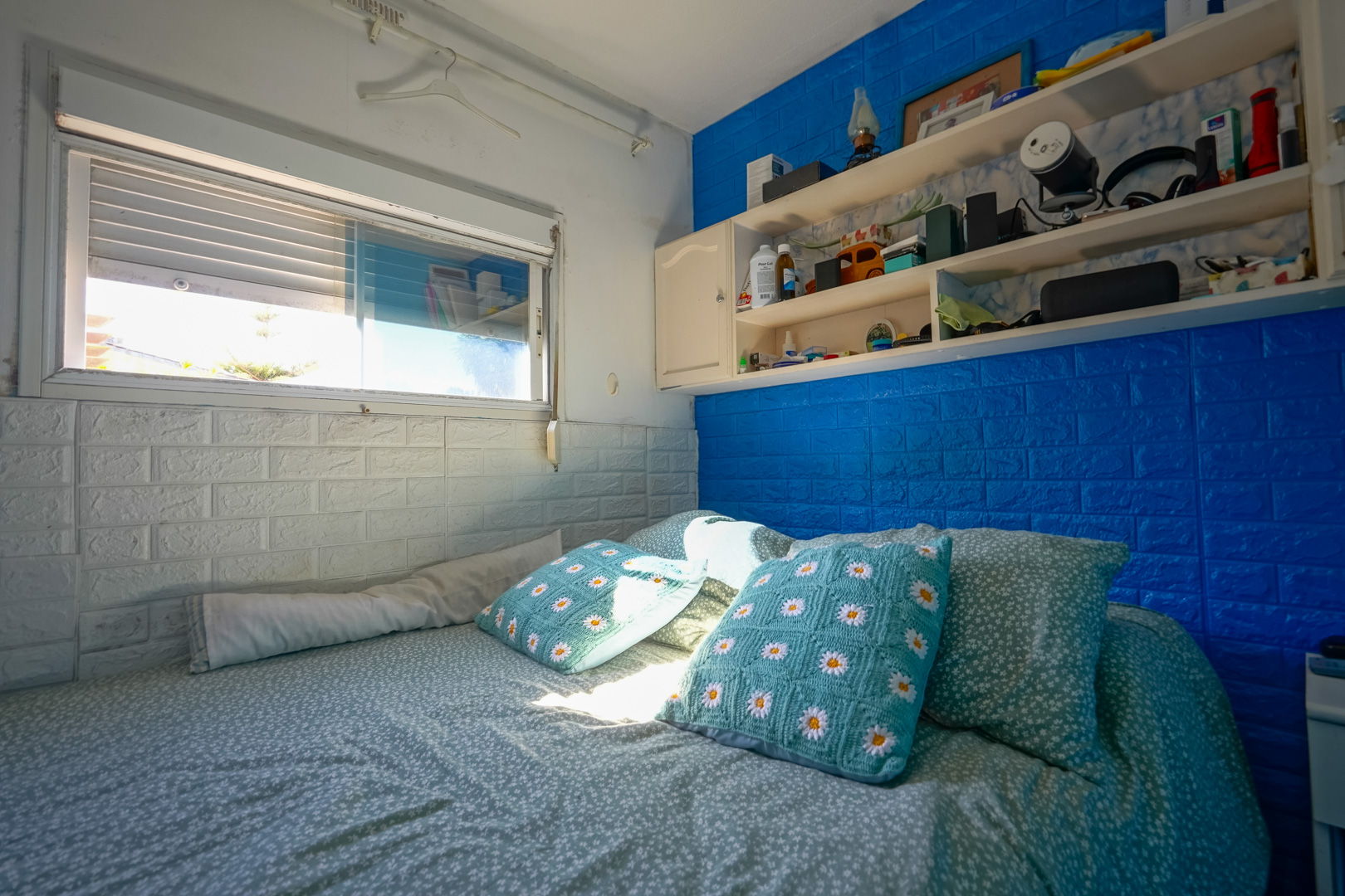 Dormitorio de la vivienda prefabricada con paredes de efecto ladrillo en azul y blanco, estanterías integradas y luz natural.