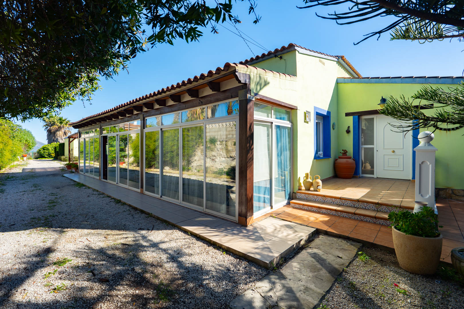 Fachada de la finca con naya acristalada, vigas de madera y porche de entrada con azulejos tradicionales y carpintería blanca.