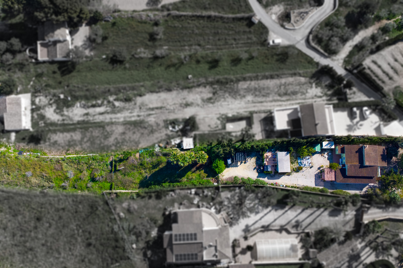 Vista aérea cenital de la finca que muestra la distribución de la vivienda principal, la zona de grava y la construcción auxiliar en la parcela rústica.