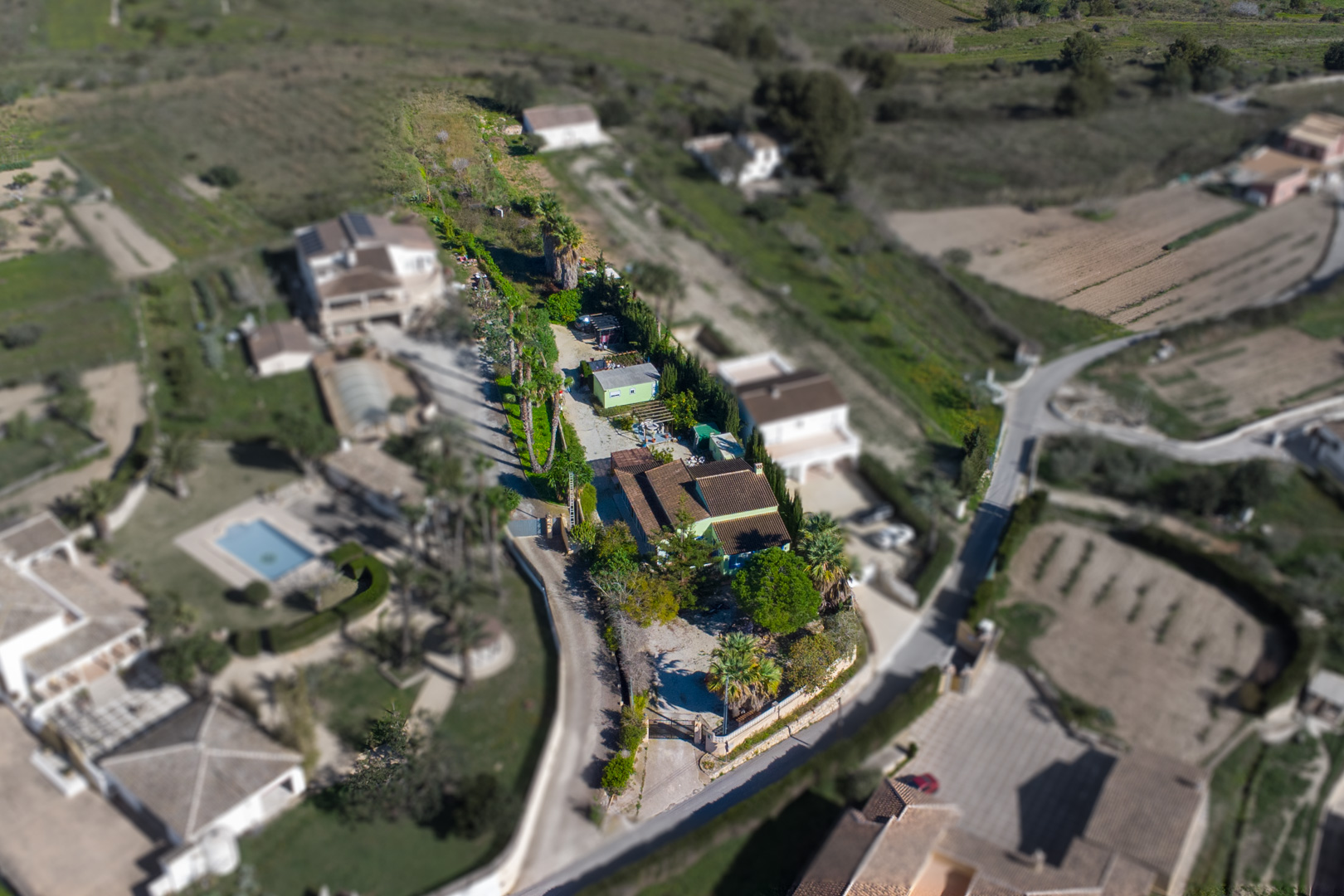 Vista aérea de la parcela rústica de 2.800 m2 que muestra la vivienda principal, la casa prefabricada independiente y el extenso terreno con palmeras.