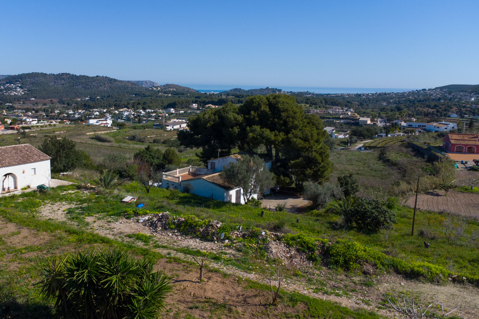Vista panorámica de la finca tradicional y su parcela rústica, destacando las vistas despejadas hacia el valle de Benitachell y el mar Mediterráneo al fondo.