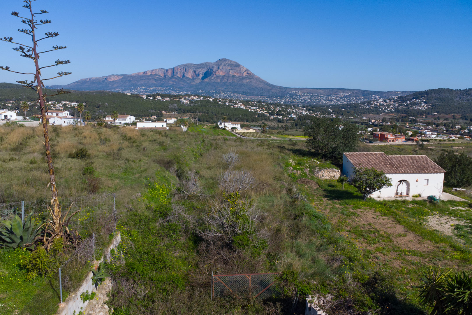 Vista panorámica desde la parcela rústica hacia el valle de Benitachell, con el imponente monte Montgó al fondo bajo un cielo despejado.