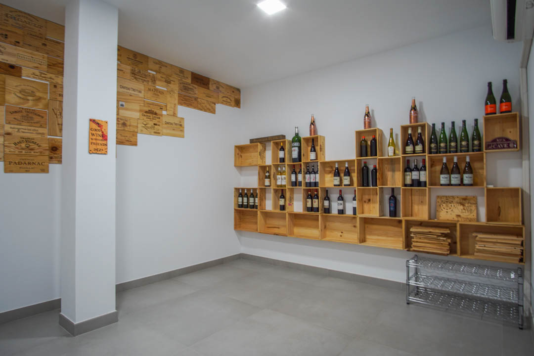Bodega privada con estanterías de cajas de madera natural y pared decorada con frontales de cajas de vino sobre suelo de gres gris.