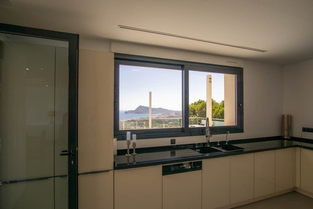 Cocina moderna con encimera de granito negro y fregadero integrado. El gran ventanal ofrece vistas panorámicas al mar y la bahía de Altea desde la zona de trabajo.