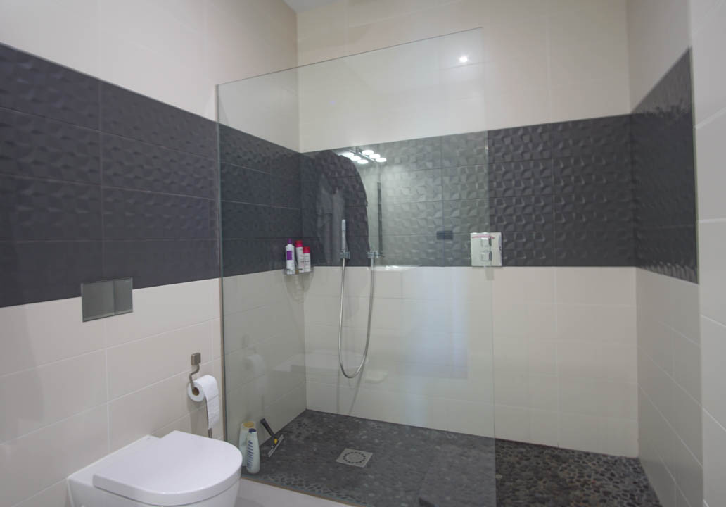 Cuarto de baño moderno con ducha a ras de suelo, mampara de cristal, suelo de cantos rodados y azulejos con relieve geométrico en contraste.