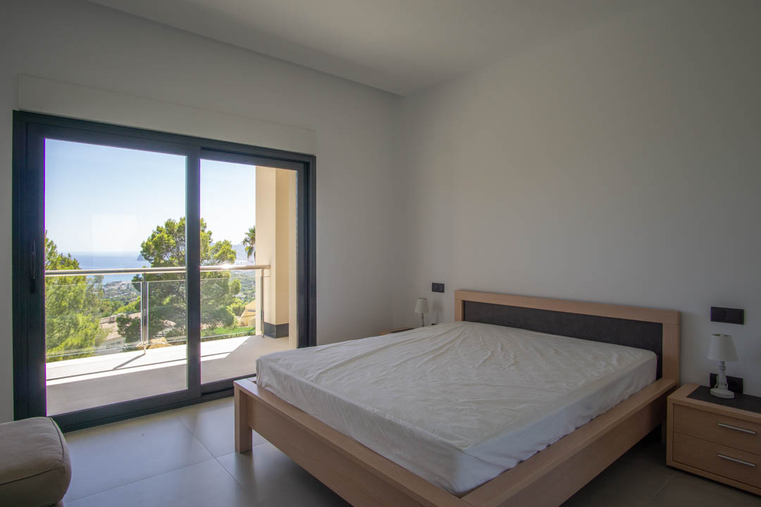 Dormitorio luminoso con cama de madera clara, acceso directo a balcón privado y vistas panorámicas al mar y entorno natural de Altea.