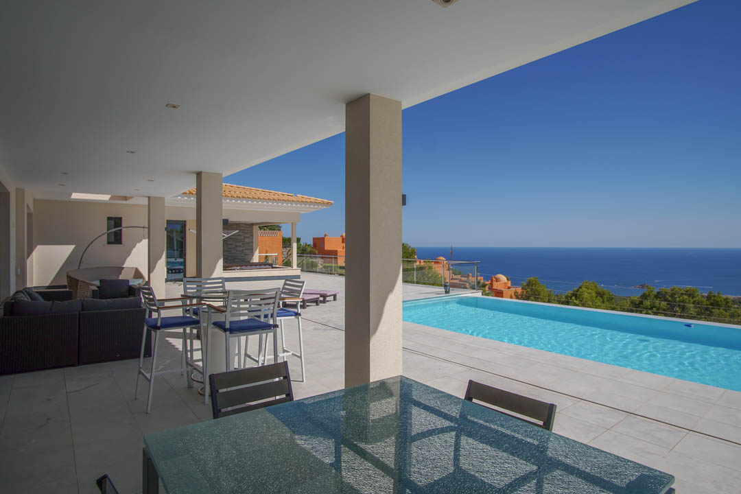 Terraza cubierta con zona de comedor exterior, piscina infinita y vistas panorámicas al mar Mediterráneo desde la Sierra de Altea.