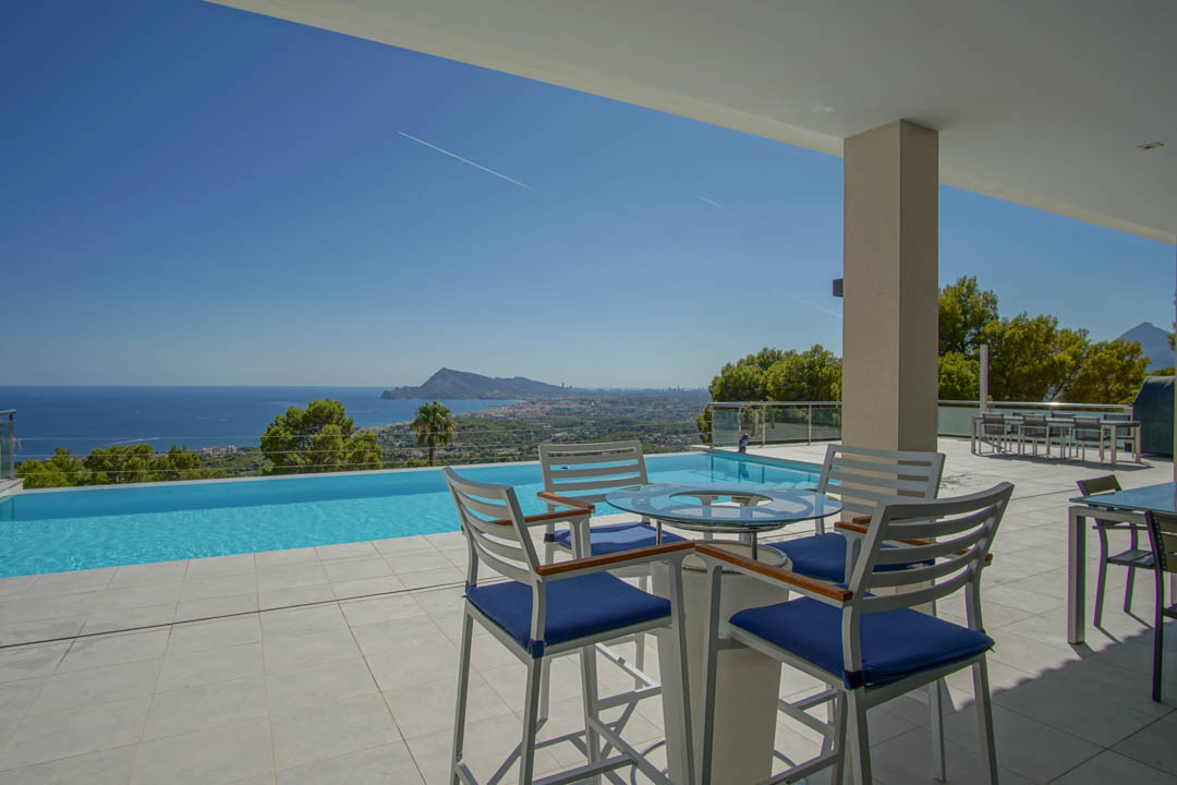 Terraza principal con piscina infinita, mobiliario exterior de diseño y vistas panorámicas a la bahía de Altea y el skyline de Benidorm.