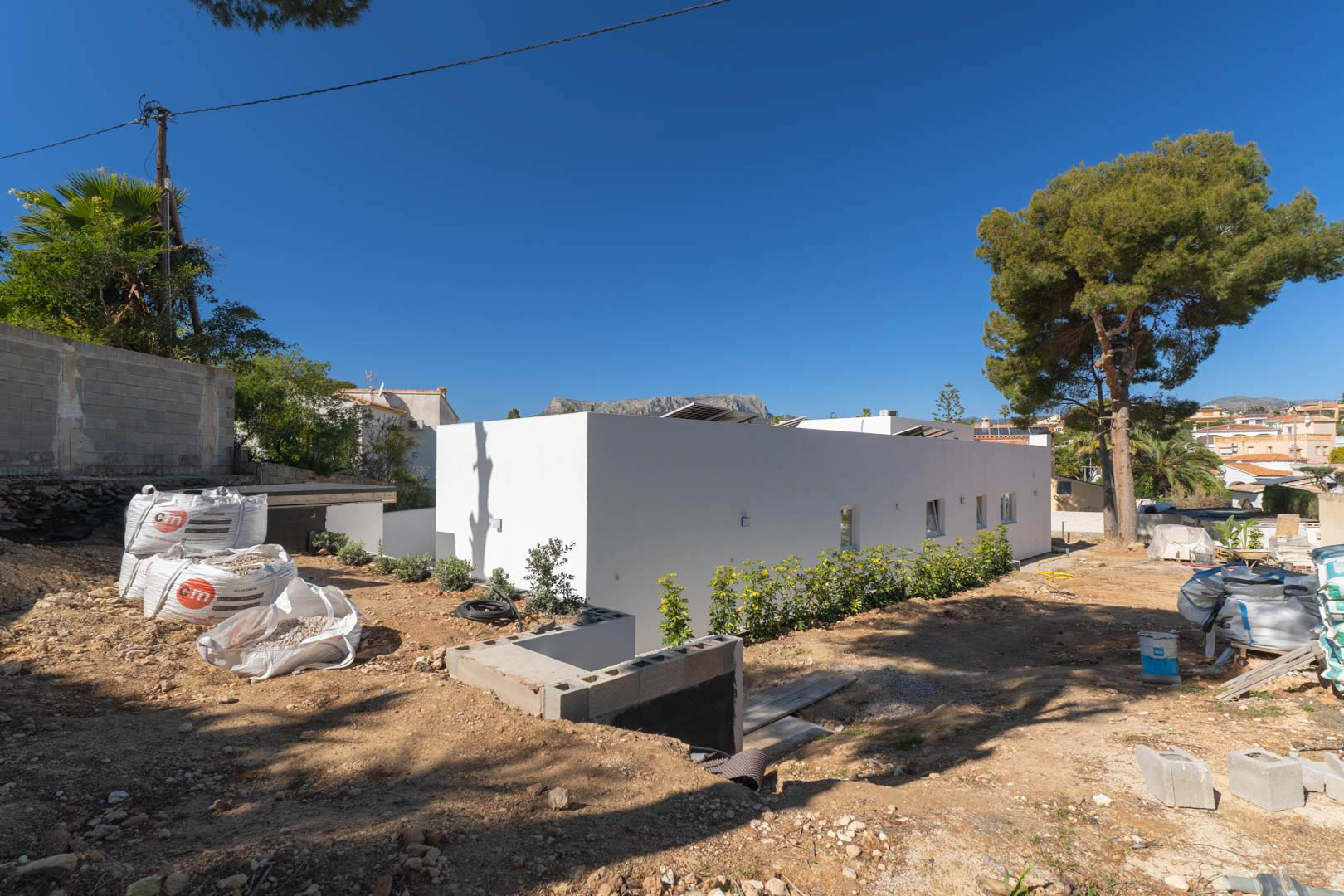 Fachada minimalista de una sola planta con paneles solares integrados. La parcela exterior se encuentra en fase de nivelación y preparación para el futuro jardín.