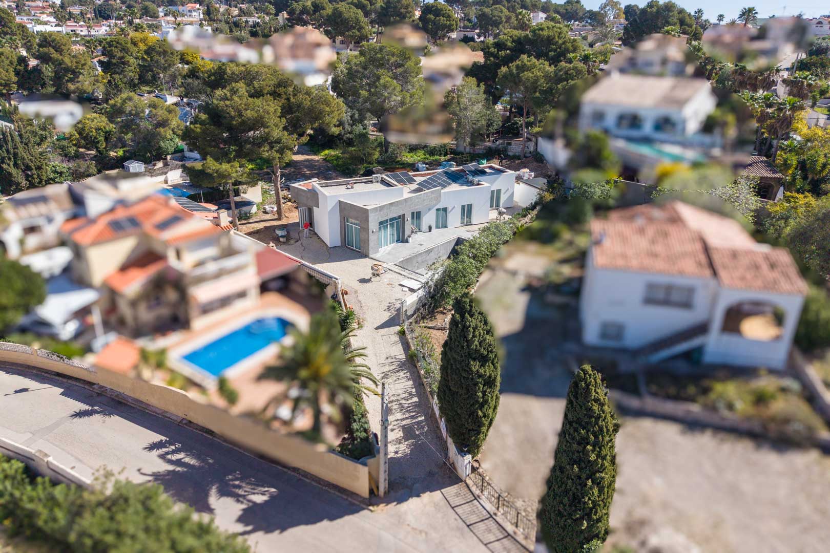 Vista aérea de la villa minimalista con paneles solares en su cubierta plana, mostrando la parcela en fase de terminación rodeada de un entorno residencial consolidado.
