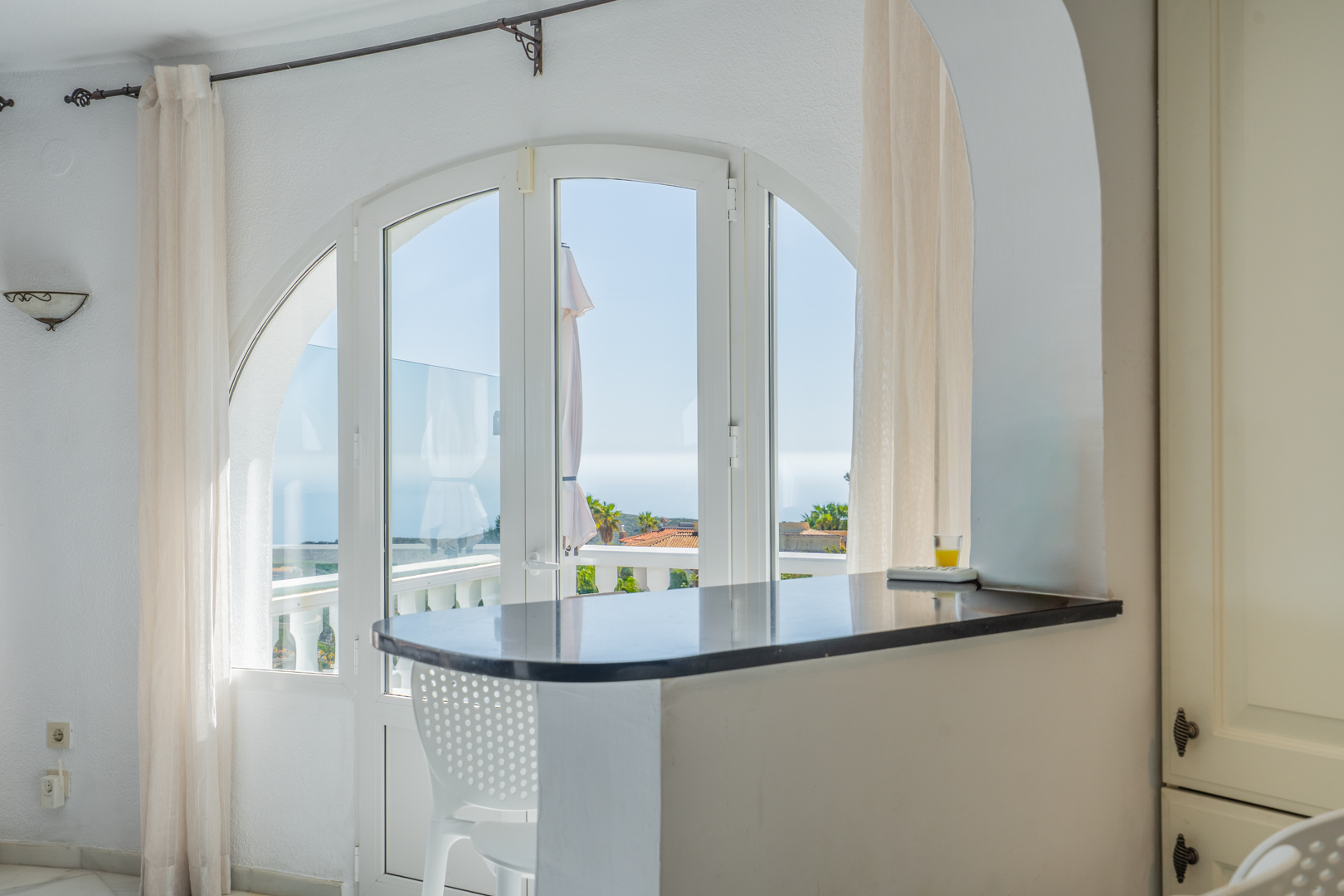 Barra de cocina en granito oscuro integrada bajo un arco, con vistas al mar a través de ventanales arqueados que dan acceso a la terraza exterior.