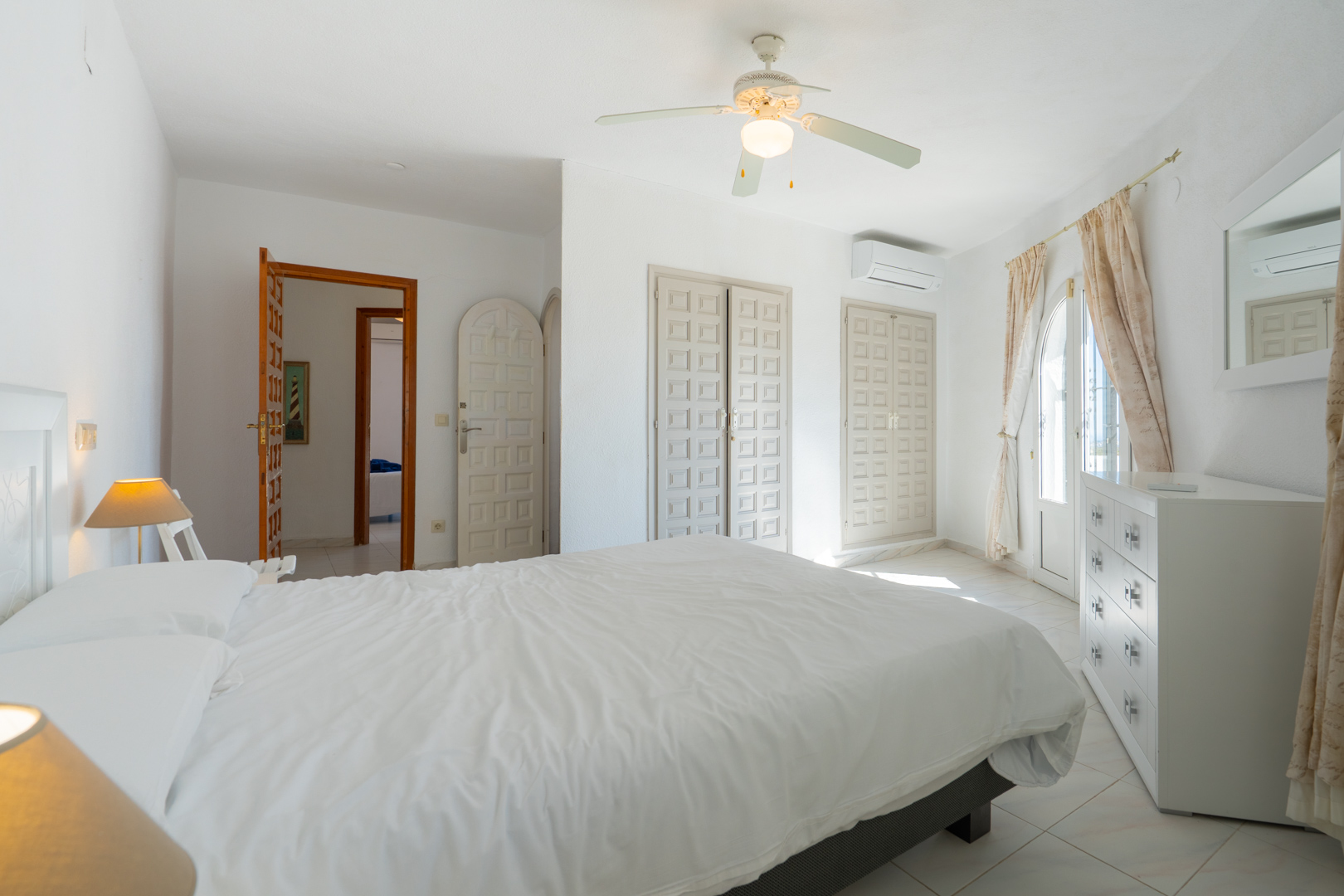 Dormitorio luminoso con armarios empotrados de estilo tradicional, aire acondicionado, ventilador de techo y acceso directo al exterior mediante una puerta acristalada.