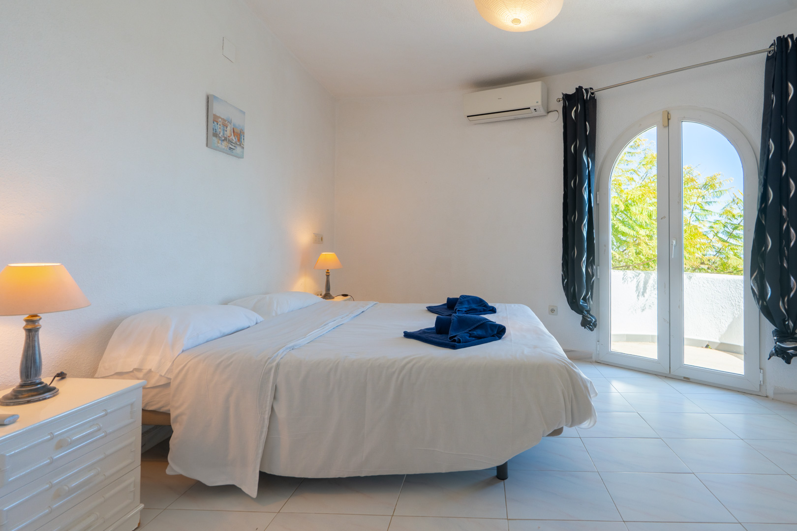 Dormitorio luminoso con cama doble, aire acondicionado y puerta de arco acristalada con acceso directo a la terraza exterior.