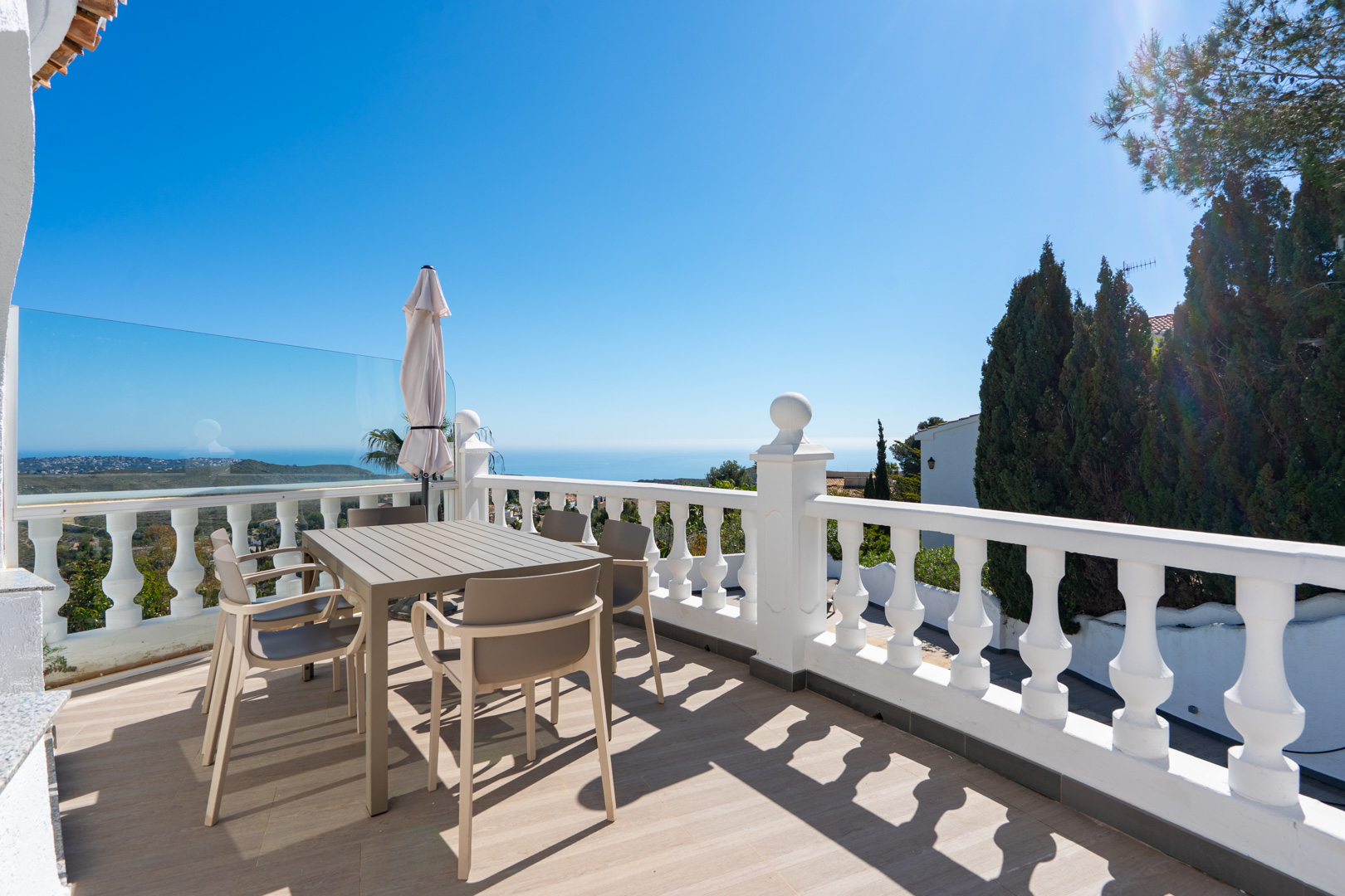Terraza superior con barandilla de balaustrada blanca, conjunto de comedor moderno y vistas panorámicas al mar Mediterráneo y al parque natural.