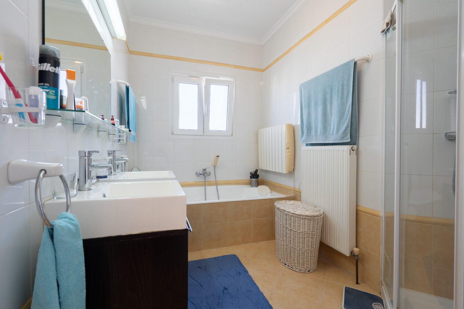 Cuarto de baño completo con lavabo doble, bañera integrada, ducha independiente y paredes alicatadas con detalles en tonos cálidos.