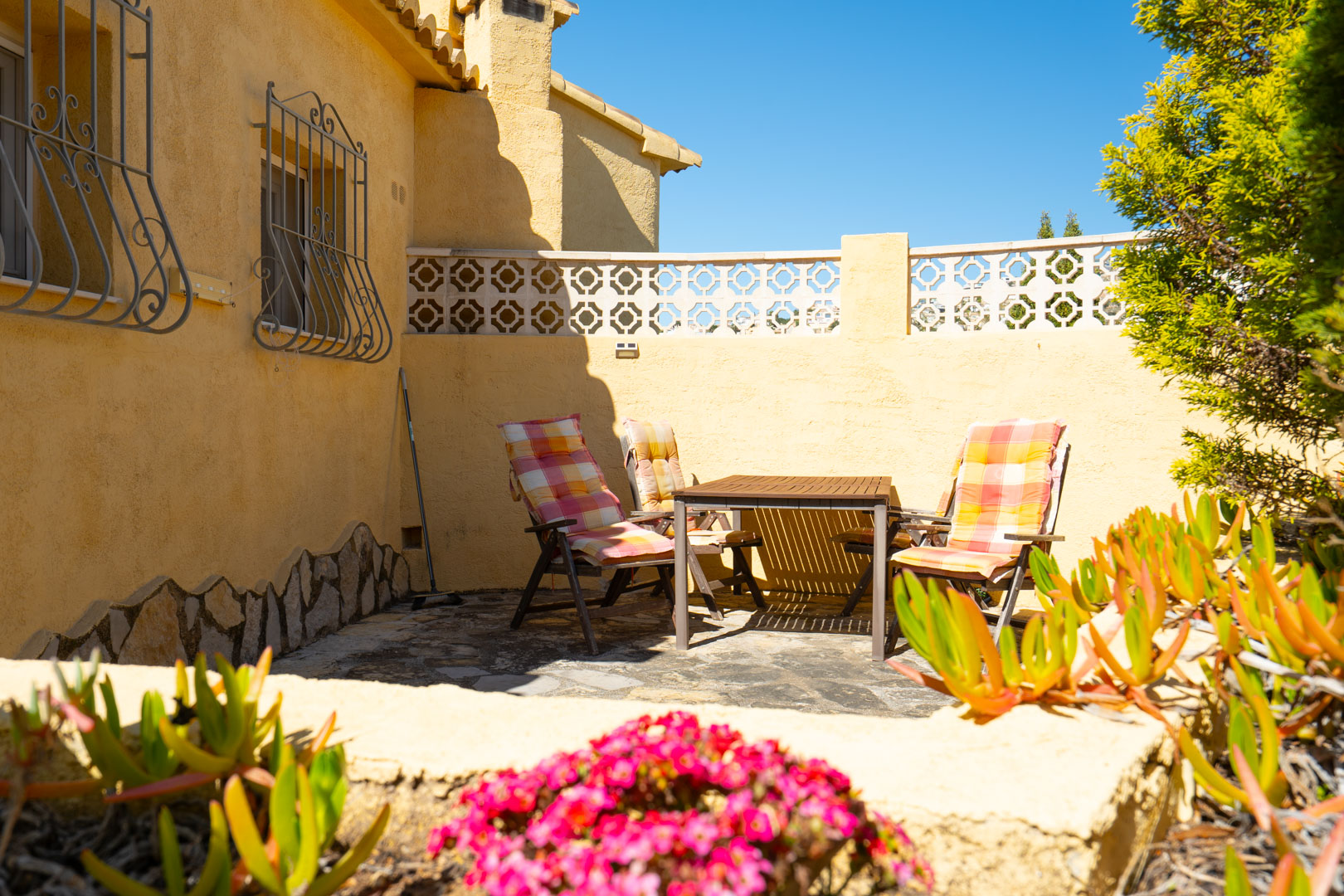 Terraza exterior con suelo de piedra natural, mobiliario de madera y fachada en tonos ocres con rejas tradicionales de hierro forjado.