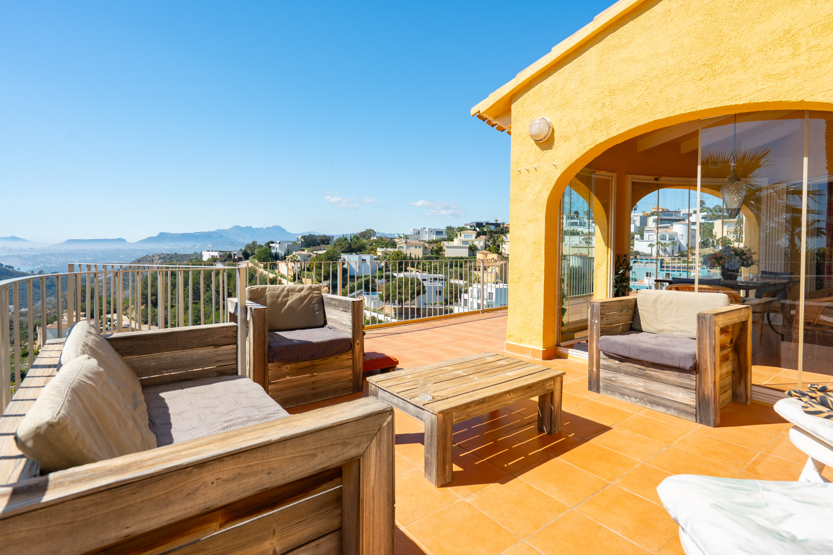 Terraza solárium con mobiliario de madera rústica, pavimentos de terracota y vistas panorámicas hacia la costa y la Sierra de Bernia.