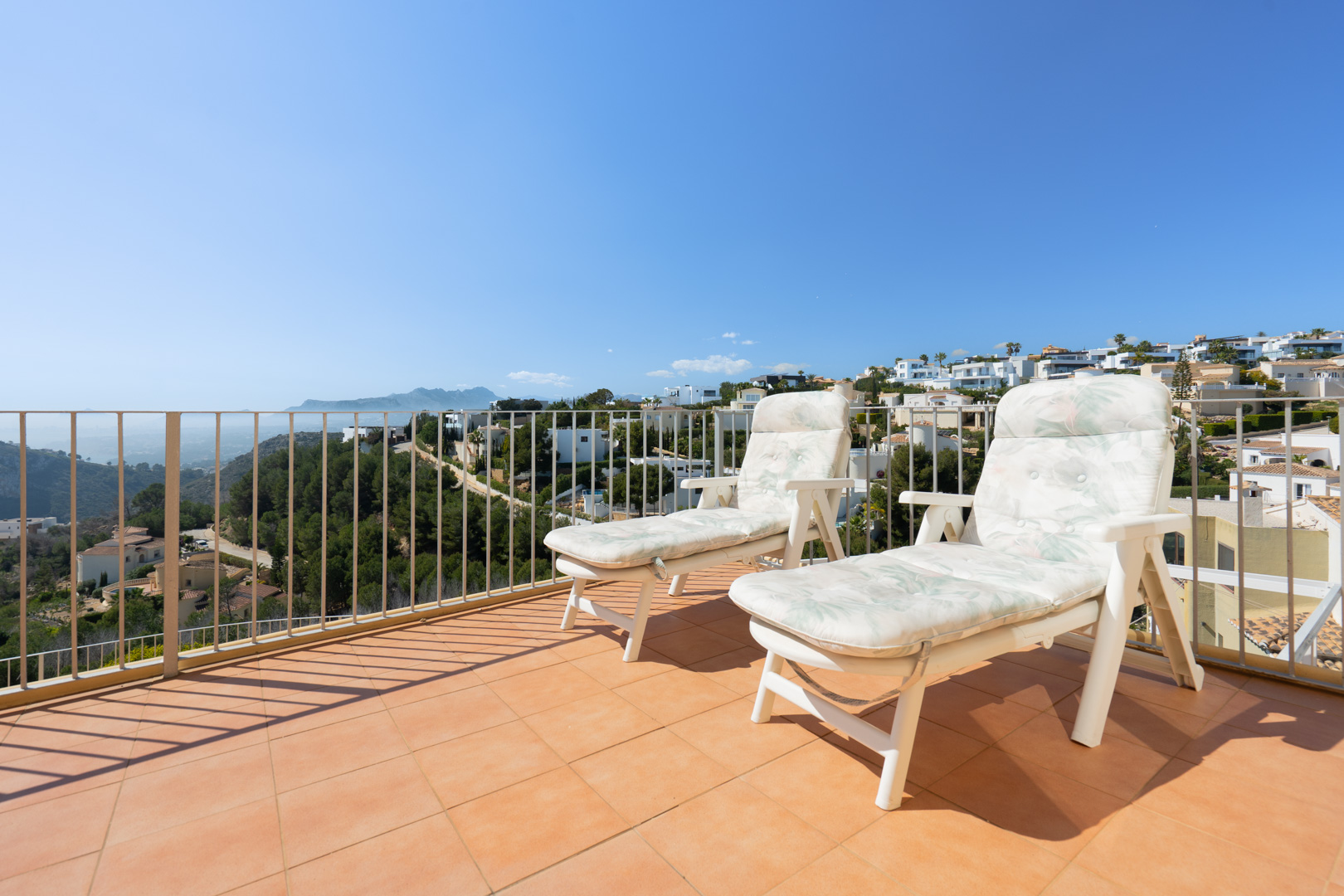 Terraza solárium con suelo de baldosas cerámicas y barandilla metálica, equipada con hamacas y vistas despejadas a la costa y las montañas de la Marina Alta.