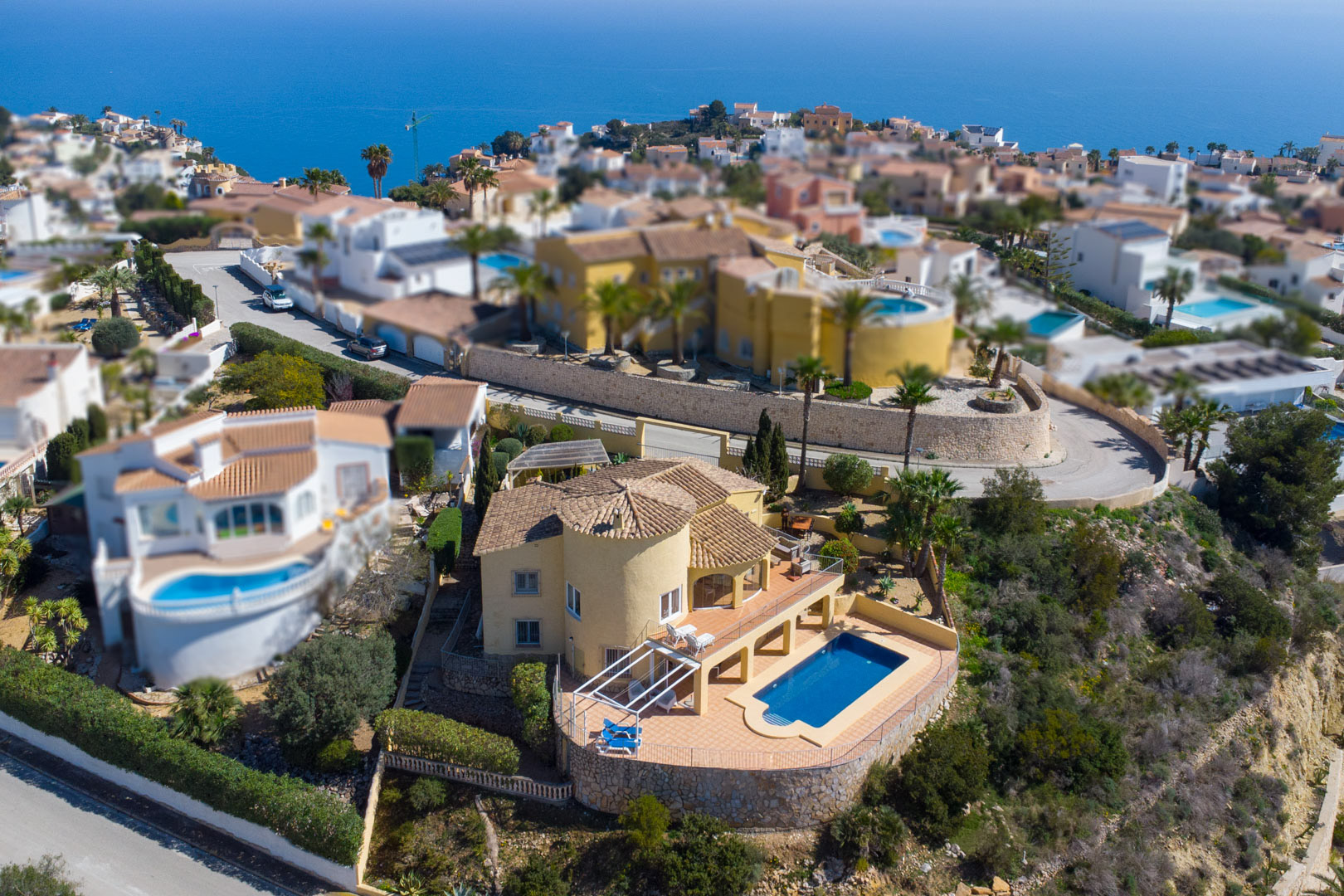 Vista aérea de la villa tradicional con fachada amarilla, torre circular y piscina privada rodeada de una amplia terraza con vistas al mar Mediterráneo.
