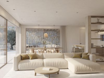Amplia sala de estar con sofá seccional claro y mesa de centro redonda. Grandes puertas de cristal dan a un patio exterior con muro de piedra natural y un olivo.