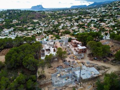 Vista aérea de construcciones de villas con cimientos de hormigón y estructuras de ladrillo, en una zona residencial verde con vistas al mar y la montaña.