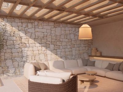 Zona de estar exterior con pared de piedra natural, pérgola de madera y un gran sofá esquinero. La iluminación ambiental y el mobiliario moderno crean un espacio acogedor.