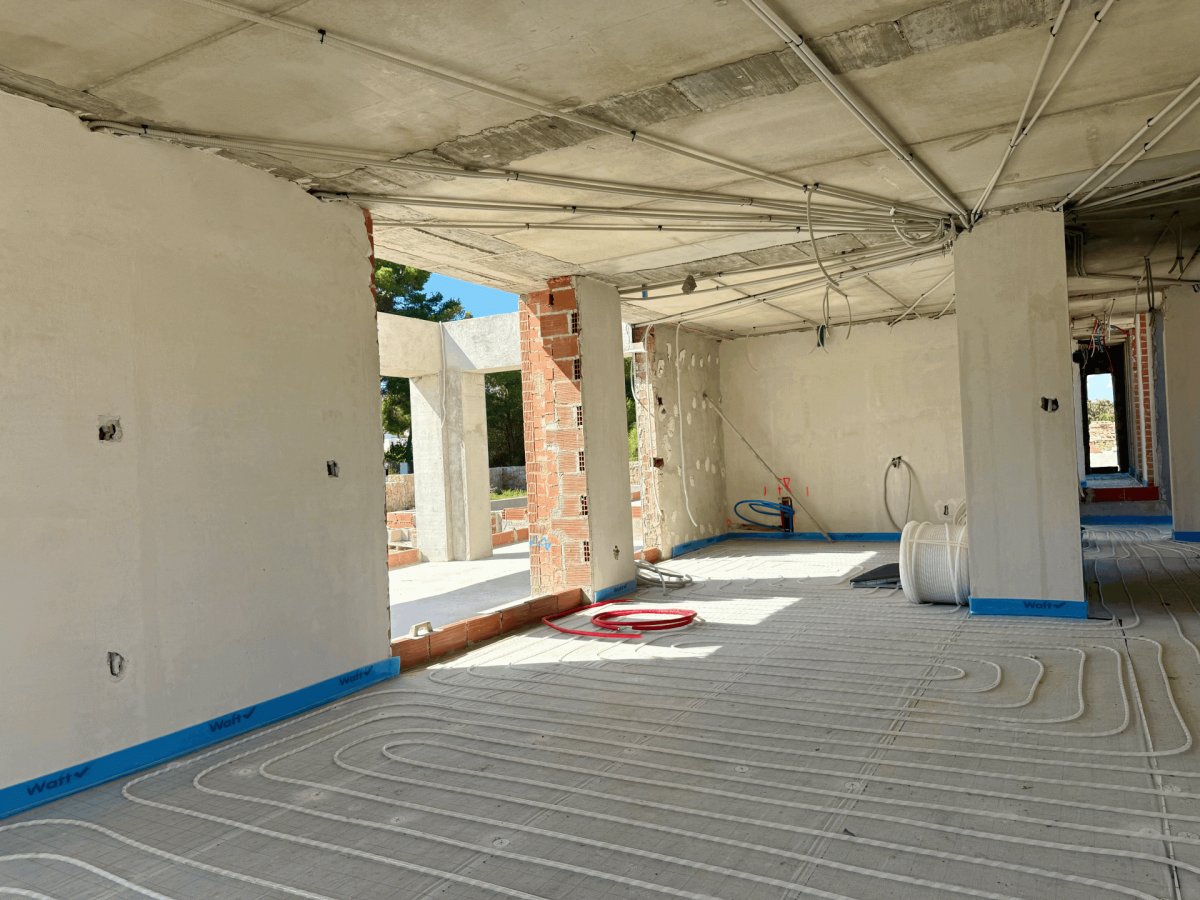 Espacio interior en construcción, mostrando la instalación de tuberías de suelo radiante sobre el hormigón. Conductos eléctricos expuestos en el techo de hormigón. Espacio interior en construcción, mostrando la instalación de tuberías de suelo radiante sobre el hormigón. Conductos eléctricos expuestos en el techo de hormigón.