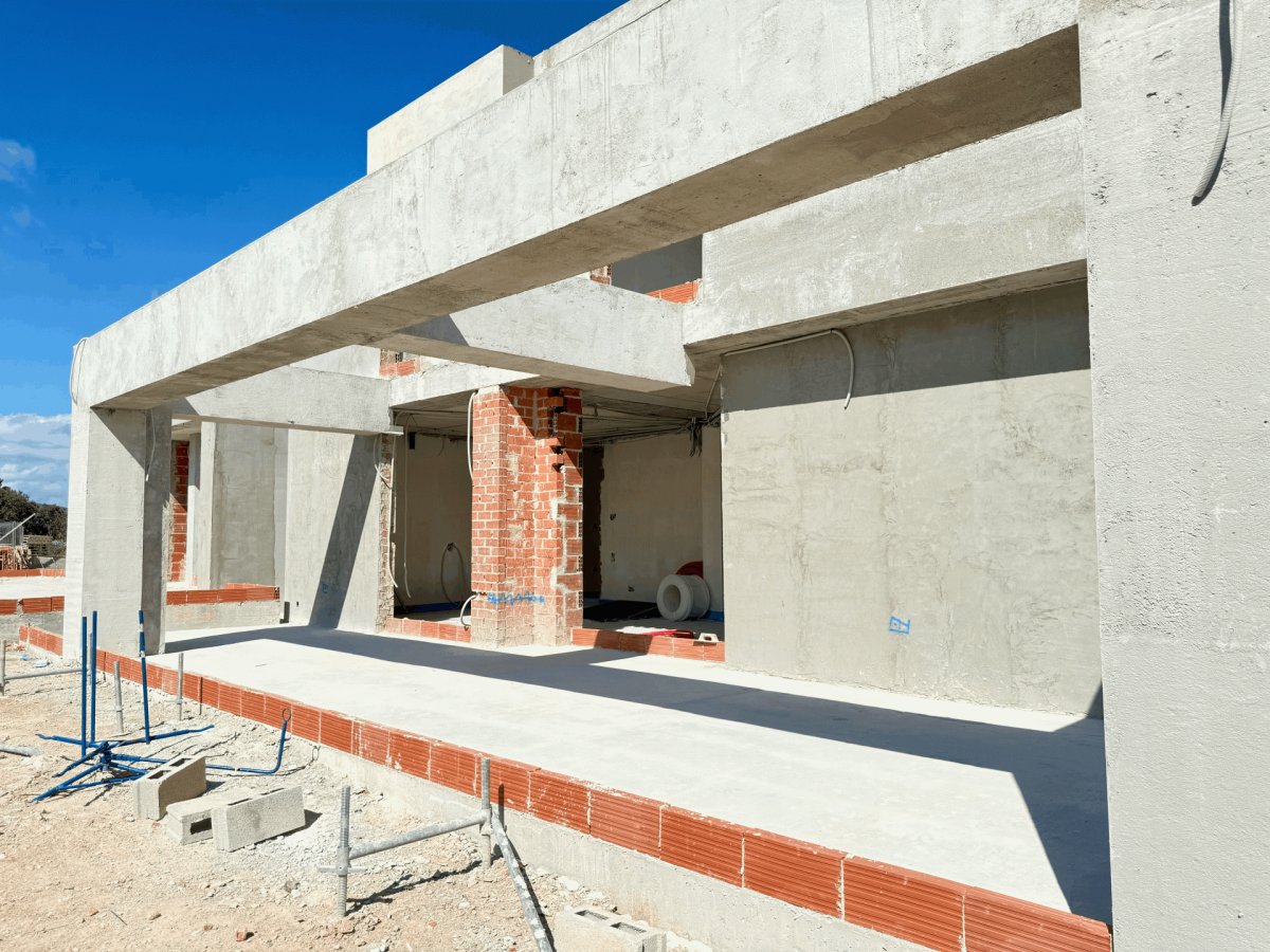 Estructura de hormigón de la villa en construcción, mostrando vigas, pilares y paredes de ladrillo visto bajo un cielo azul claro. Estructura de hormigón de la villa en construcción, mostrando vigas, pilares y paredes de ladrillo visto bajo un cielo azul claro.