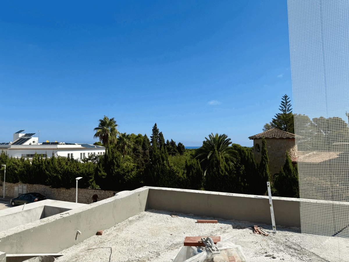Terraza en construcción con vistas parciales al mar Mediterráneo y exuberante vegetación. Se aprecian detalles de obra y un cielo azul despejado. Terraza en construcción con vistas parciales al mar Mediterráneo y exuberante vegetación. Se aprecian detalles de obra y un cielo azul despejado.