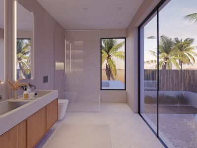 Baño moderno con doble lavabo de madera, ducha con mampara de cristal y suelo de guijarros. Grandes ventanales ofrecen vistas a un patio privado con palmeras.