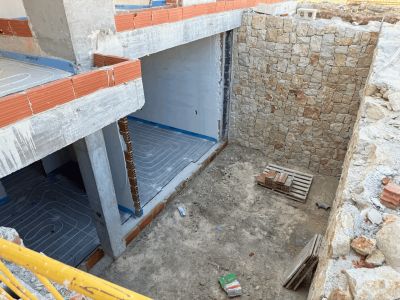 Construcción de sótano con instalación de suelo radiante visible, muros de hormigón y una pared de piedra natural en proceso.
