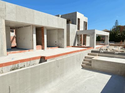 Estructura de hormigón de una villa moderna en construcción, mostrando el diseño de la piscina privada vacía con sus escaleras y el cielo azul despejado.