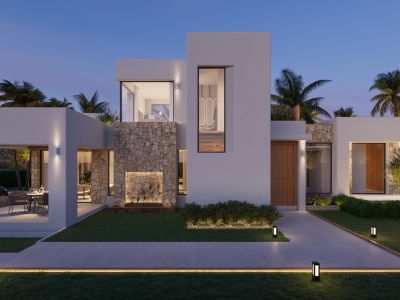 Exterior de villa moderna al atardecer, con fachadas blancas, detalles de piedra natural y comedor exterior cubierto iluminado. Caminos y jardines presentan iluminación integrada.