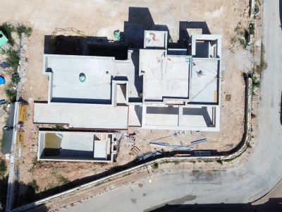 Vista aérea de la villa en fase de construcción, mostrando la estructura de hormigón y la excavación de la piscina privada junto a la carretera.
