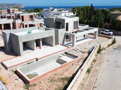 Vista aérea de una villa moderna en construcción, mostrando su estructura de hormigón y una piscina privada parcialmente edificada. Se aprecian vistas lejanas al mar y la montaña.