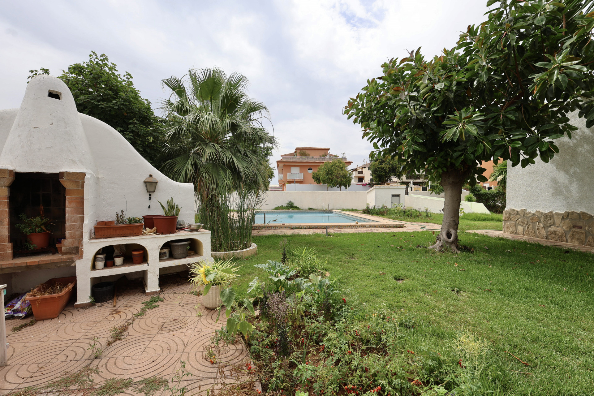 Barbacoa de obra con estantes en jardín con piscina y vegetación.