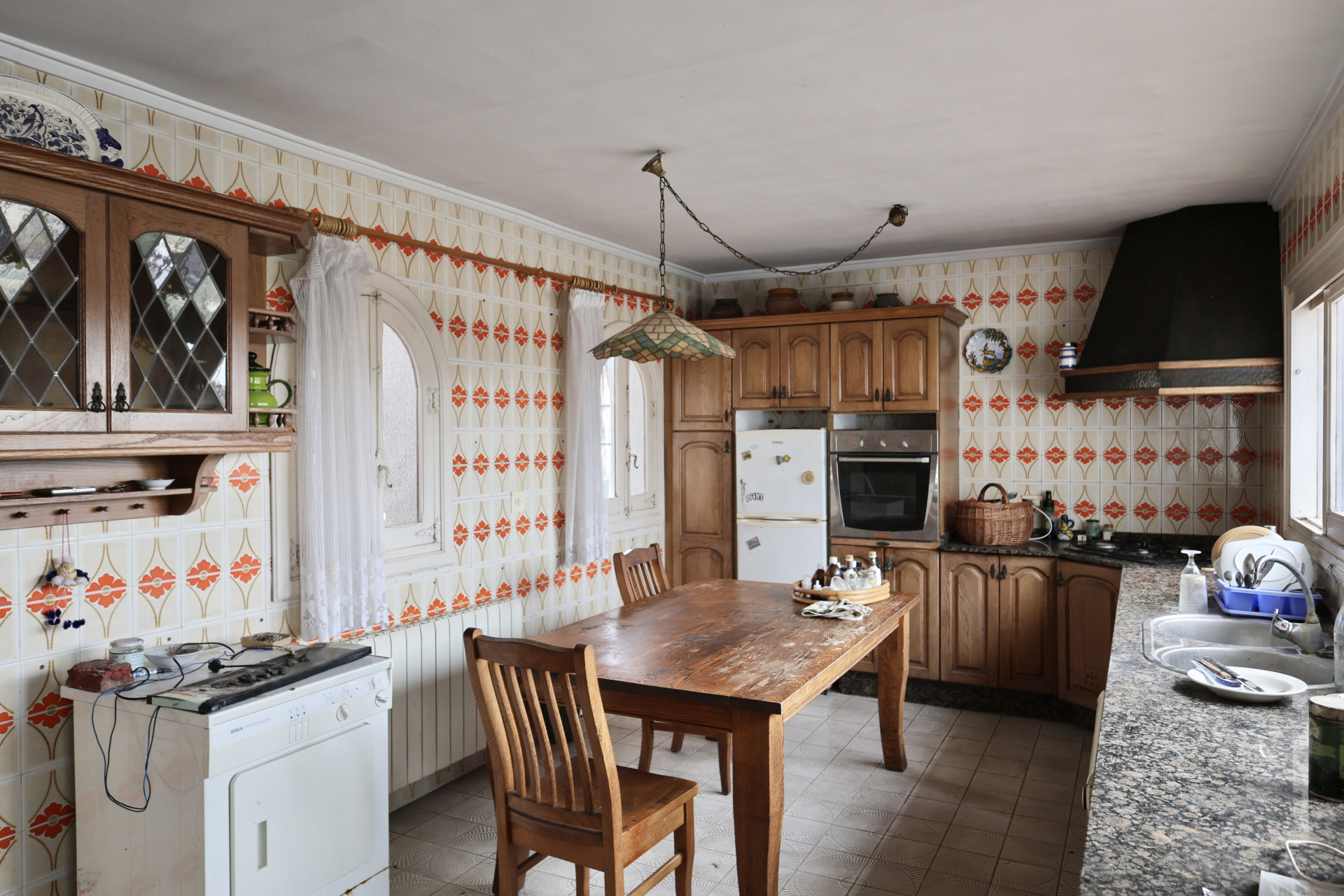 Cocina con azulejos estampados y mobiliario de madera, a reformar.