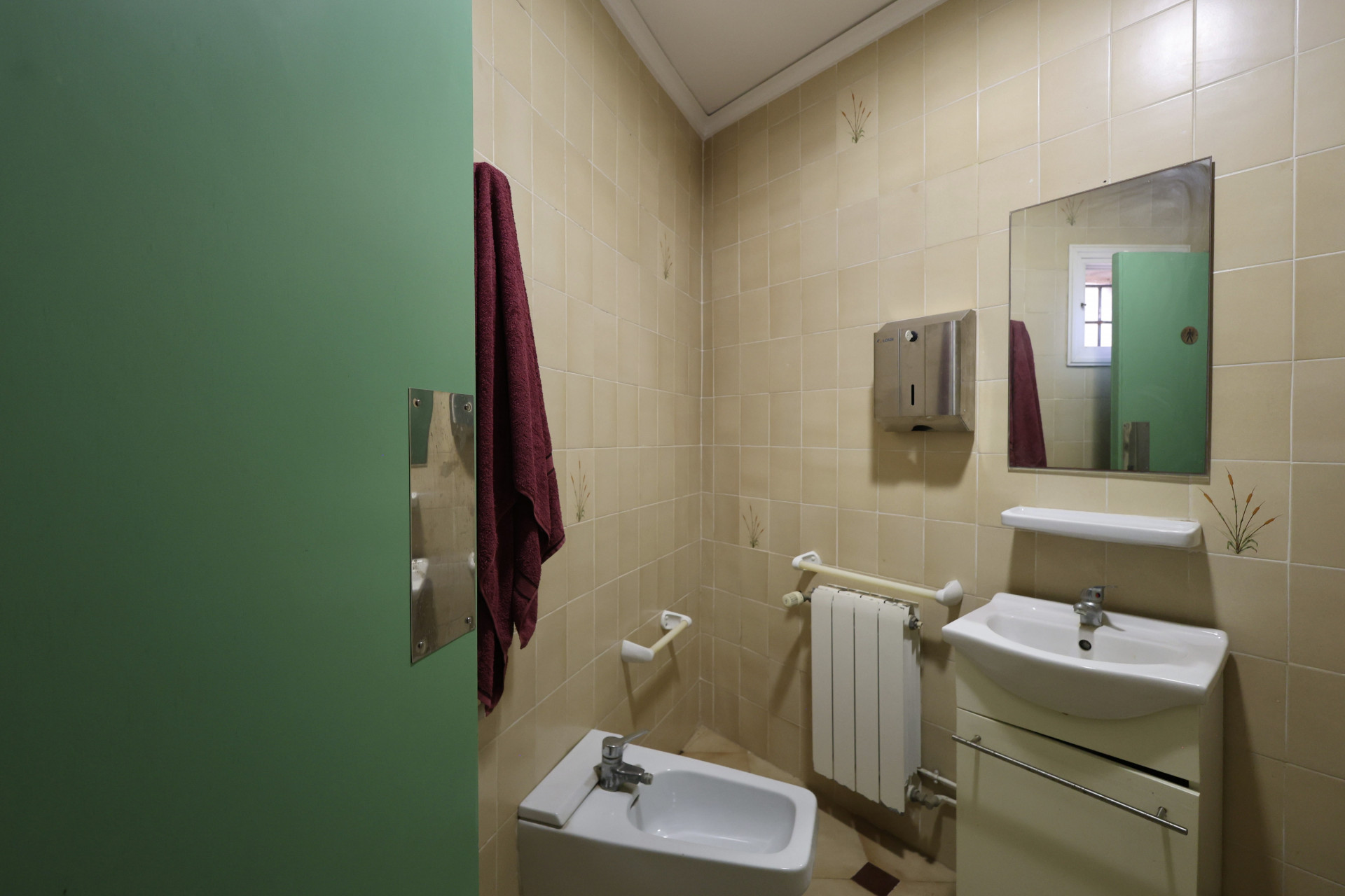 Cuarto de baño con azulejos color crema, bidet blanco y puerta verde.