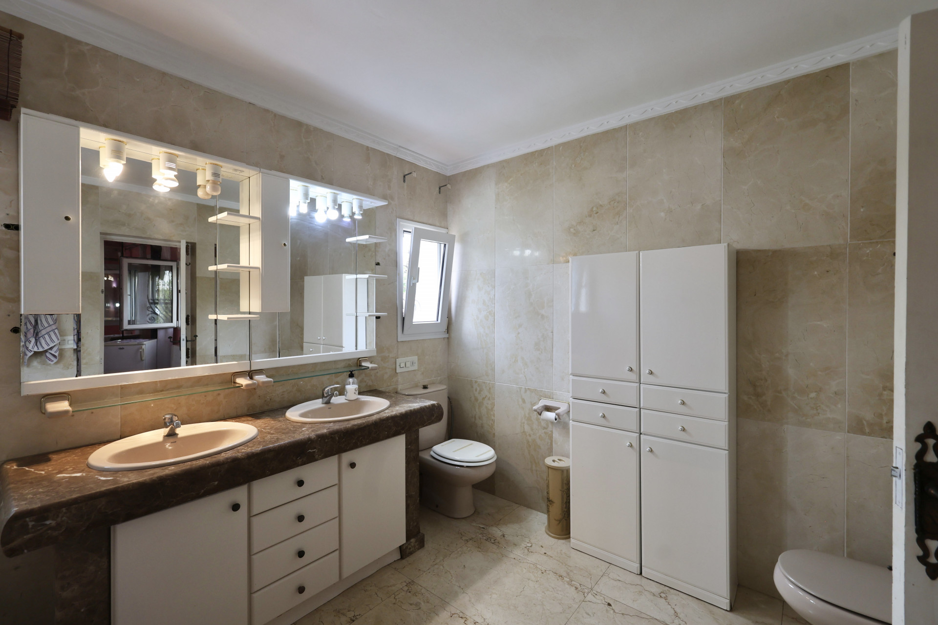 Cuarto de baño con lavabo doble, encimera de mármol y armarios blancos.