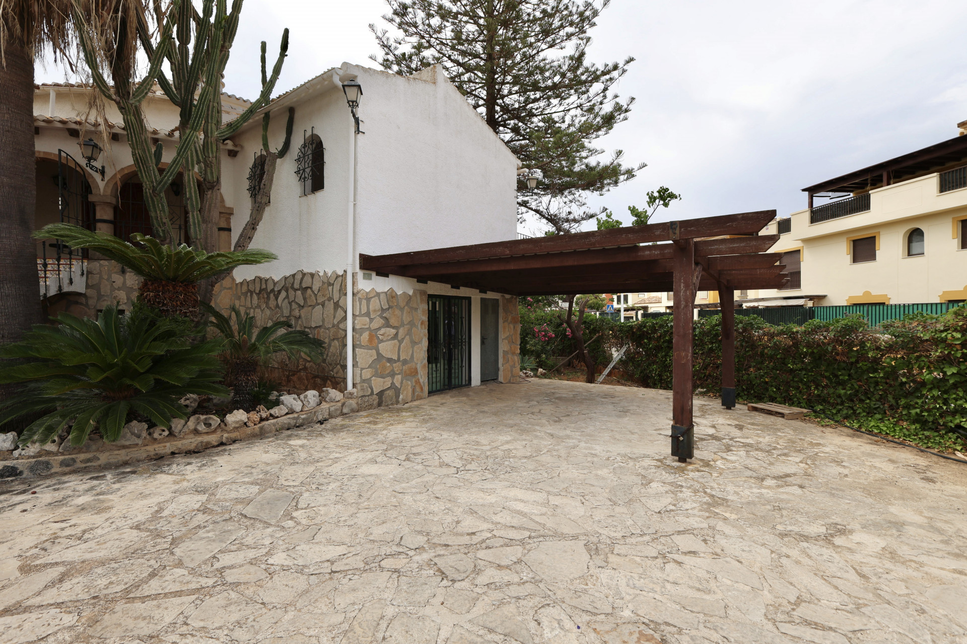 Entrada de villa con suelo de piedra irregular y garaje cubierto con estructura de madera.
