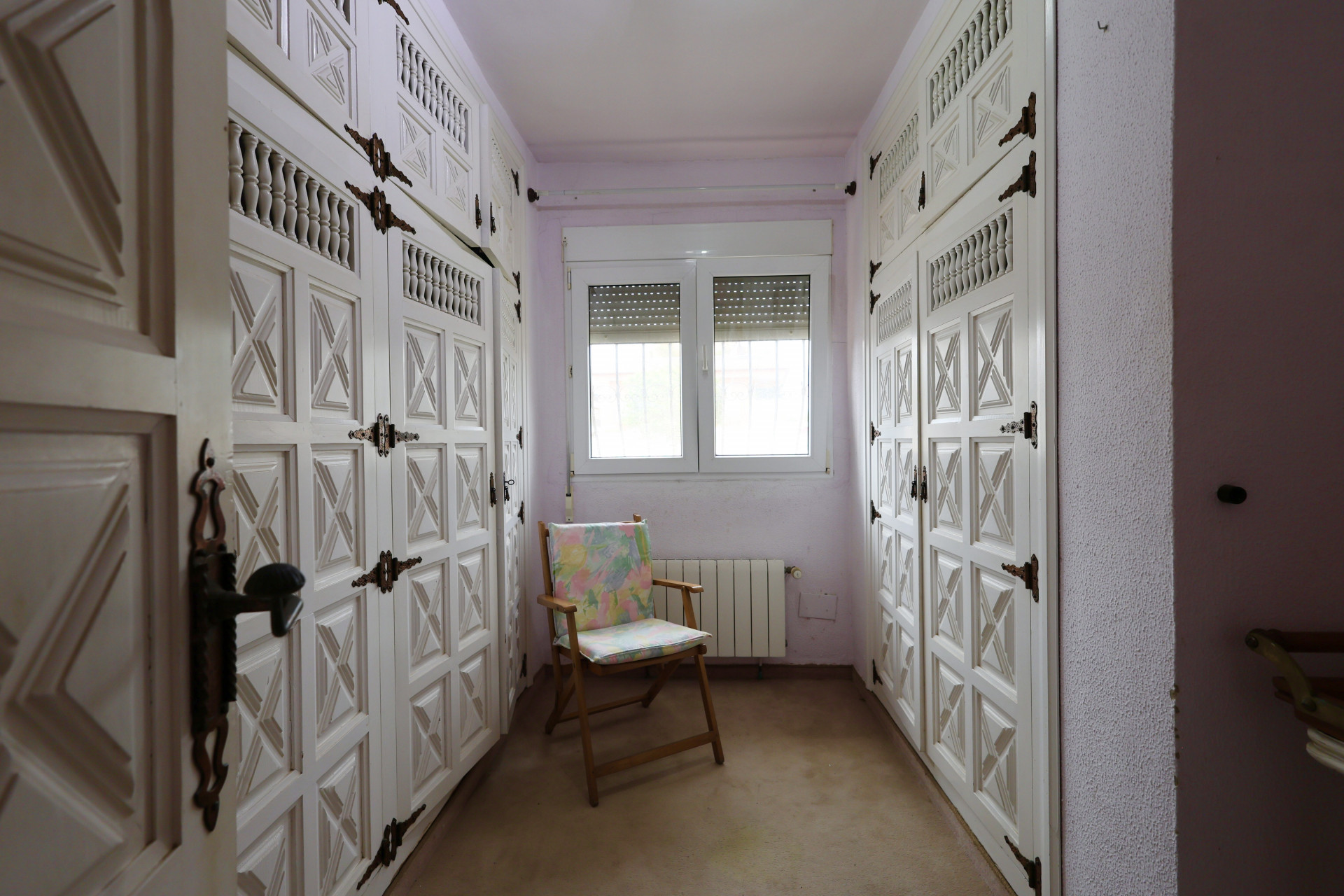Vestidor con armarios empotrados blancos y herrajes de hierro, iluminado por una ventana.