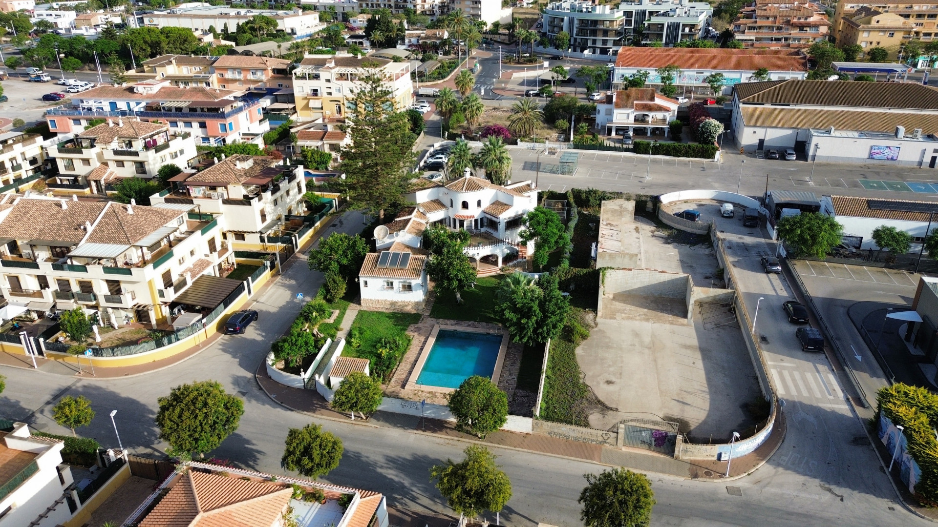 Vista aérea de la villa con piscina azul rodeada de jardines y edificios urbanos en Jávea.