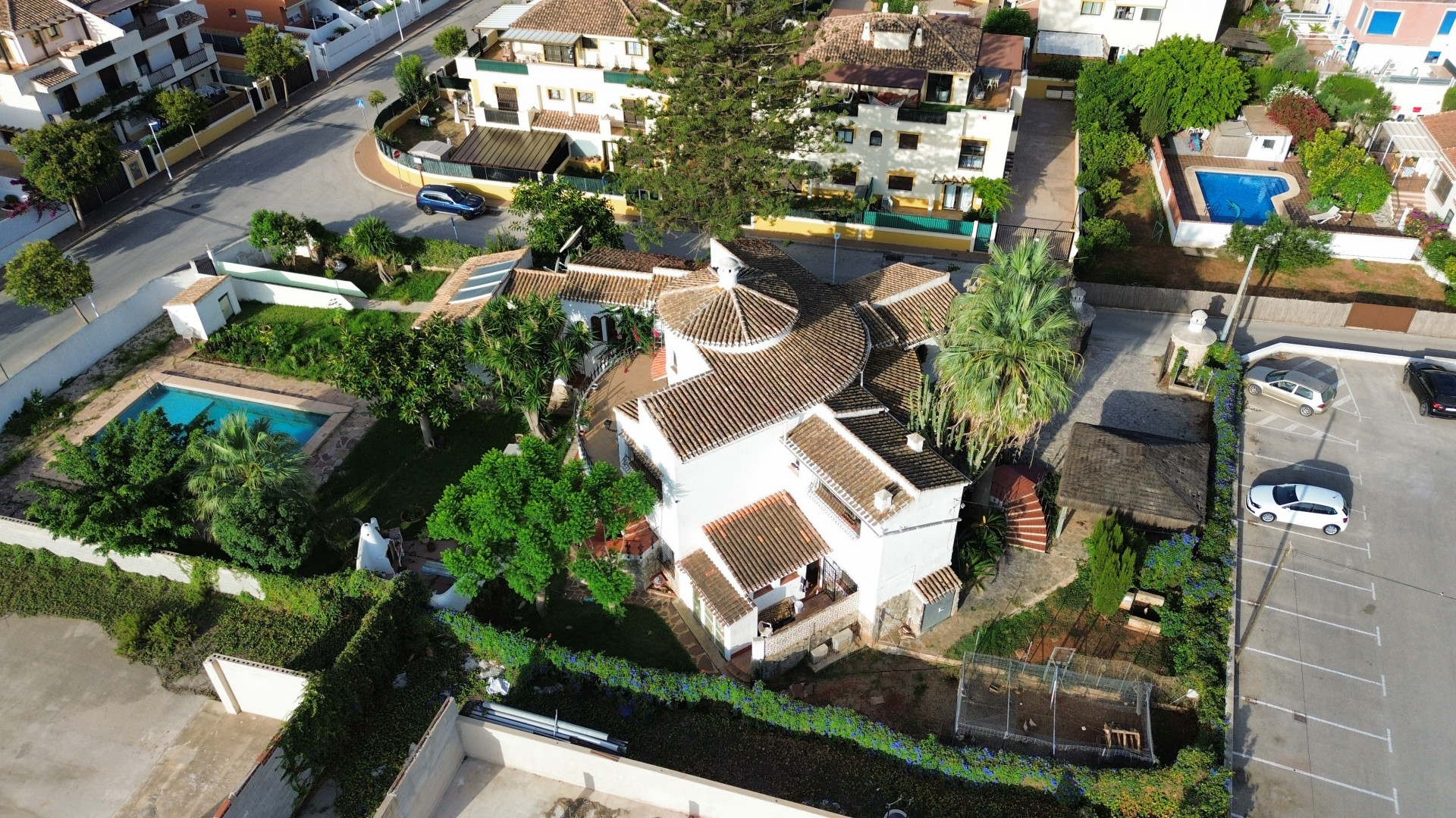 Vista aérea de la villa con tejado de tejas, piscina rodeada de vegetación y aparcamiento adyacente.