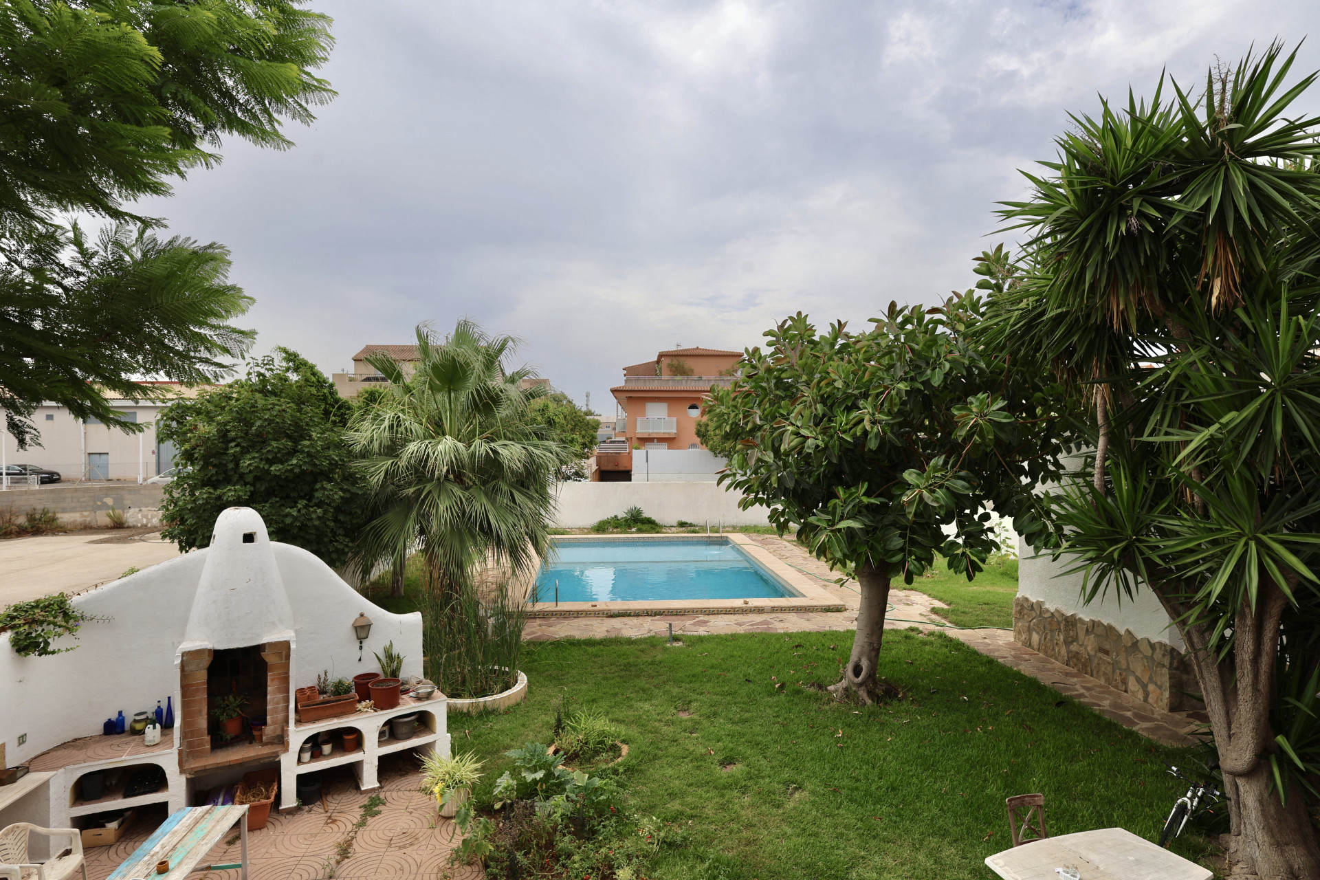 Vista del jardín con piscina, barbacoa de obra y vegetación abundante en Jávea.