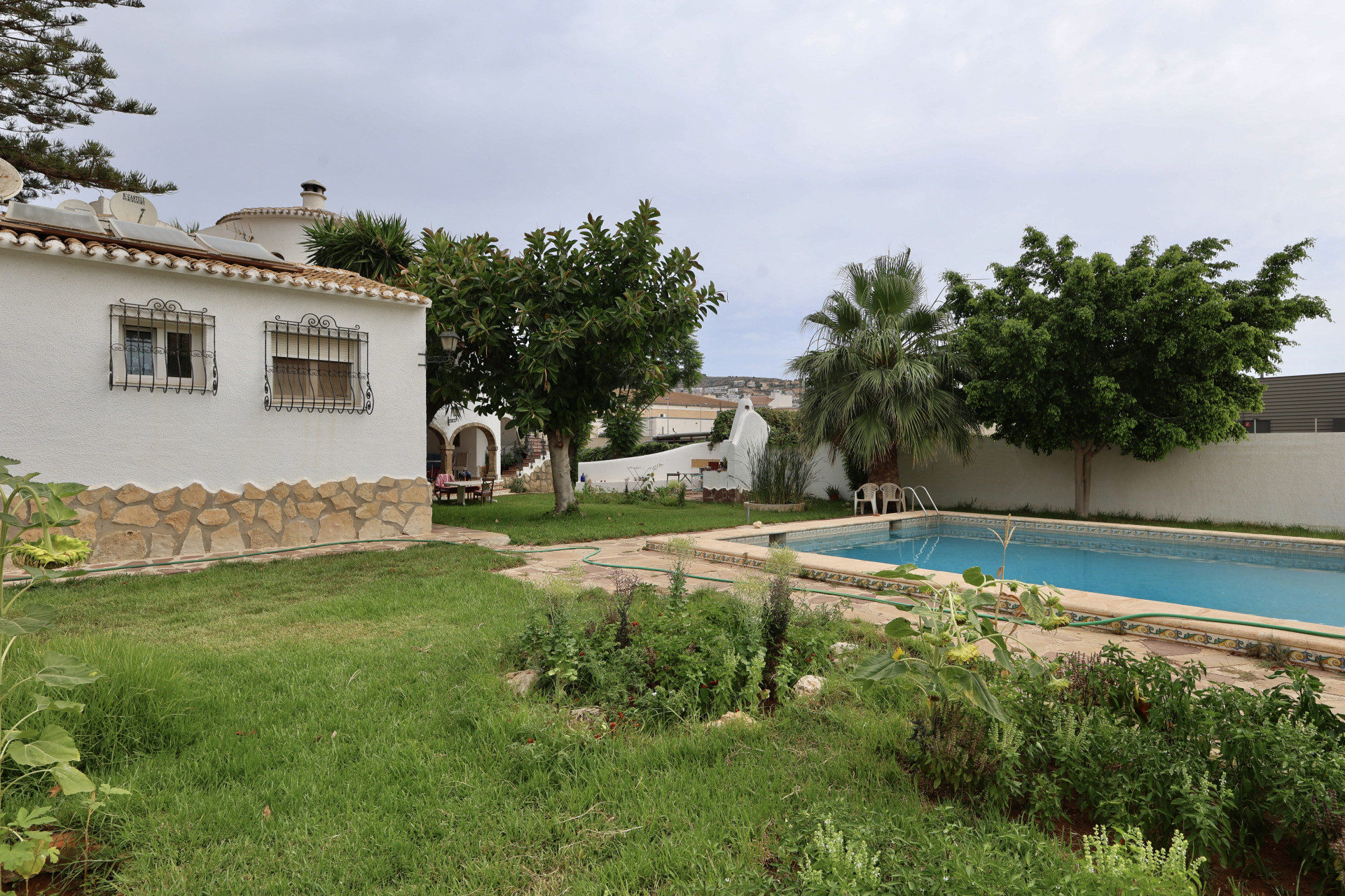 Vista del jardín con piscina rectangular y fachada de villa con detalles de piedra.